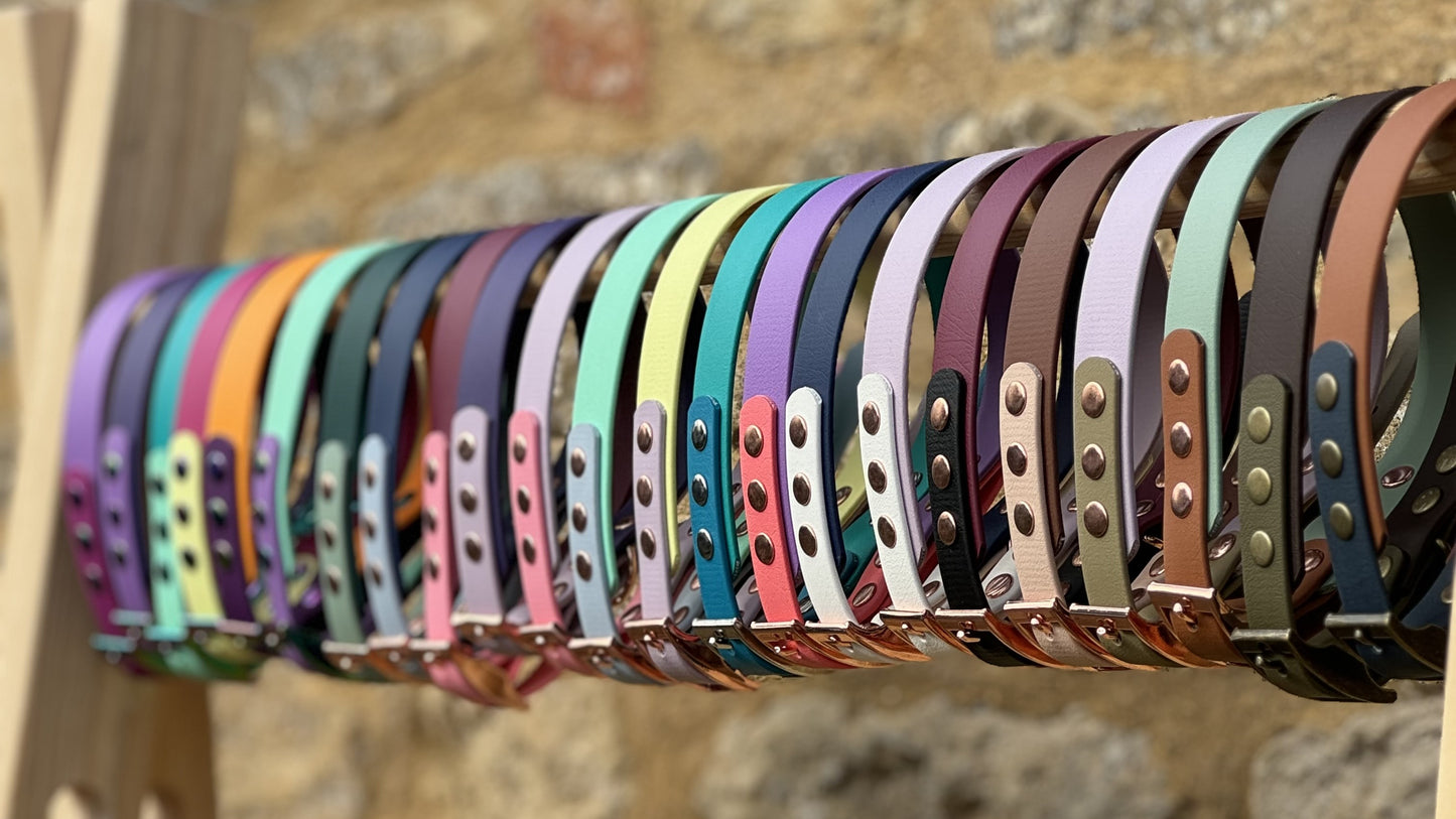 Row of colorful dog collars on a wooden stand with a stone wall background.